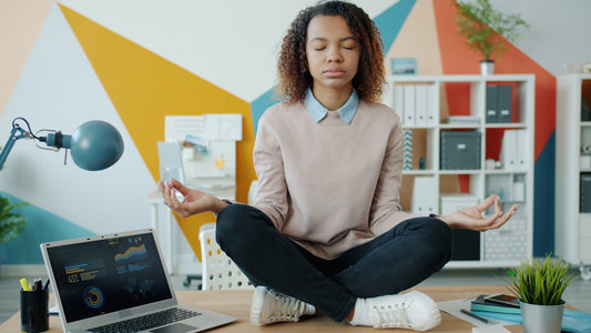 Woman meditating at a desk with laptop.